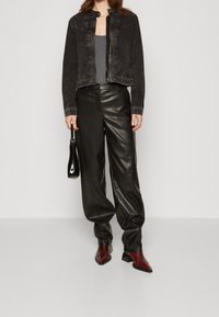 Svart denimjacka med en figurnära design, grå top, svarta läderbyxor med vida ben och spetsiga röda stövlar, håller en liten svart väska.