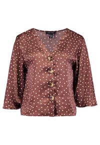 Brun satinblus med vita prickar, V-ringning och tre stora knappstängningar. Har löst sittande, långa ärmar.