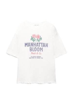 Valkoinen puuvillapaita, jossa on grafiikka pinkeistä ruusuista ja "MANHATTAN BLOOM" sinisellä, sekä lisäteksti pienemmällä fontilla alla.