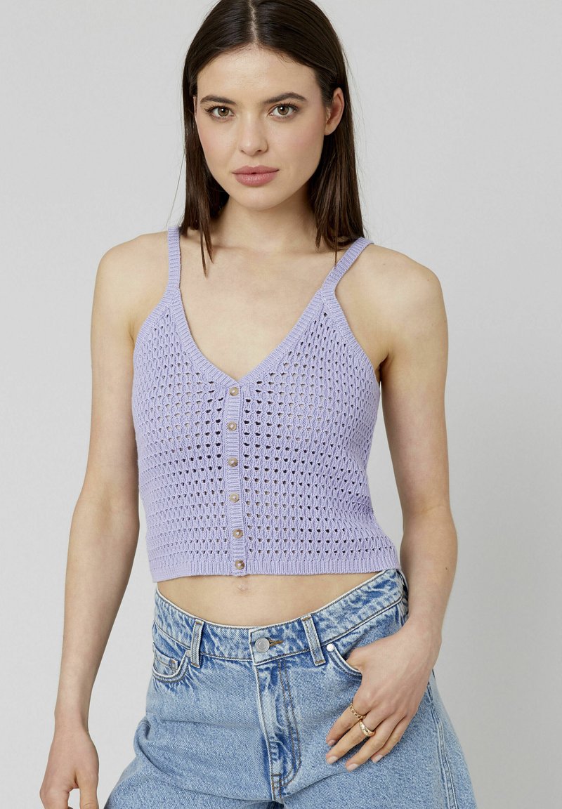 Top court en lilas avec une texture tricotée, doté d'une fermeture à boutons à l'avant et de fines bretelles. Associé à un short en denim taille haute.