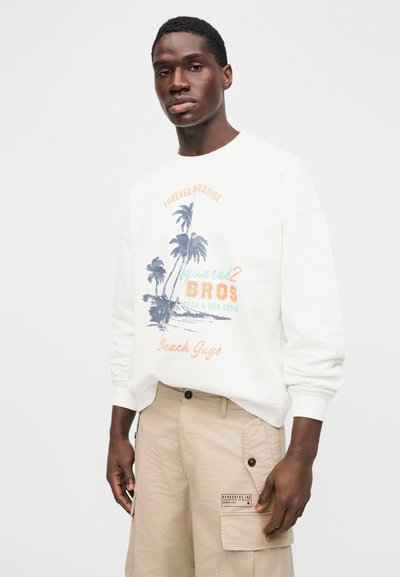 Λευκό φούτερ με γραφικό σχέδιο που απεικονίζει φοίνικες σε μπλε, πορτοκαλί και βεραμάν αποχρώσεις, συνδυασμένο με μπεζ cargo σόρτς και λεπτομέρεια με ετικέτα.