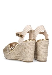 Sandalias de cuña con un tacón de cuerda trenzada, correas de tela de color beige claro con un acento dorado y un diseño de punta abierta.