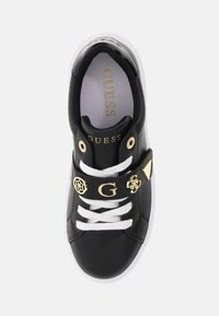 Schwarze synthetische Sneaker mit weißen Schnürsenkeln und Sohle, ausgestattet mit einem breiten Riemen, der mit goldenen Akzenten und einem Logo verziert ist. Schlichte Innengestaltung, abgerundete Zehenform.