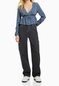 Blusa floreale a maniche lunghe con scollatura a V e laccio davanti; abbinata a pantaloni cargo neri con cuciture bianche a contrasto e tasche laterali.