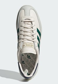 Białe skórzane sneakersy z zielonymi akcentami w postaci trzech pasków, okrągłym noskiem, płaskimi sznurówkami oraz wzorzystą wkładką z logo.