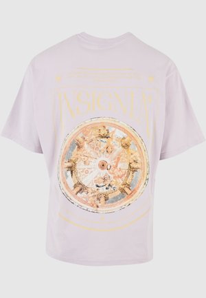 T-shirt in cotone lilla con una grande grafica rotonda dettagliata caratterizzata da disegni ornate e la parola "INSIGNIA" in grassetto giallo.
