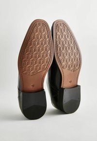 Schwarze Ledersohlenschuhe verfügen über eine braune sechseckige Musterung an der Unterseite und schwarze Gummifersenakzente mit der Größenangabe 42.
