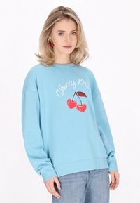 Ljusblå sweatshirt med en körsbärsgrafik och texten "Cherry Me", med avslappnad passform och ribbade muddar. Bärs med avslappnade jeans.