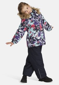 Färgglad blomstermönstrad vinterjacka med huva med pälsdetalj, i kombination med mörkblå snöbyxor och svarta kängor.