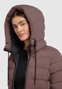 Puffjakke i dæmpet mauve, med stor hætte, lynlåslukning og lodret quiltning. Blød tekstur med snoretræk-detaljer.