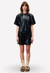 Zwart nubuck leren top met korte mouwen, gecombineerd met bijpassende shorts, met een relaxte pasvorm. Gecontrasteerd met beige sokken en leopardenprint clogs.