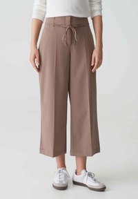 Bruine wijde broek met een trekkoord in de taille, gemaakt van zachte stof. Gecombineerd met witte sneakers met grijze accenten.