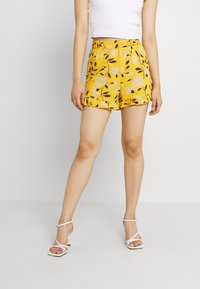 Gele bloemen shorts met een ontspannen pasvorm, een elastische tailleband en een gerimpelde zoom. Het patroon heeft witte bloemen en bruine bladeren.