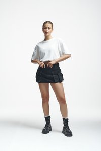 Camiseta blanca corta, falda de mezclilla negra de tiro alto con bolsillos frontales y botas de combate negras con cordones y suelas gruesas.