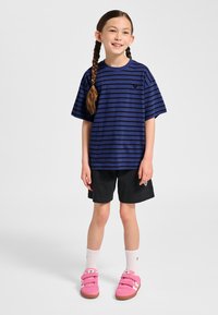 Navyblauw gestreept T-shirt met korte mouwen, gecombineerd met zwarte short en roze sneakers met klittenband. Heeft een klein logo op het shirt.