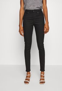 Jeans negros de corte ajustado con una cintura de altura media, que presentan un diseño clásico de cinco bolsillos y una textura de tela suave. Combinados con sandalias blancas.