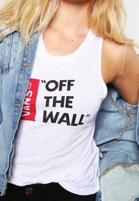 Bílé tílko s nápisem "VANS OFF THE WALL" v černé a červené barvě, doplněné svetrem z lehkého modrého denimu. Měkká látka a volný střih.
