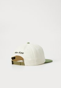 Hatt med en kremfarget stoffkropp og grønn skjerm. Funksjoner inkluderer brodert "Roller Golf"-logg og plastjusterbar stropp bak.