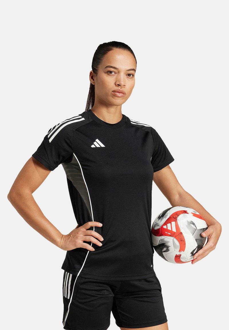 Maglia atletica nera con maniche corte e accenti bianchi ai lati, abbinata a pantaloni corti neri. Nella mano viene tenuto un pallone da calcio.