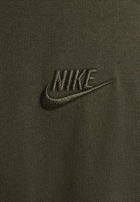 Olivegrön textil med ribbad struktur och en broderad svart Nike-logotyp, som visar en enkel och ren design.