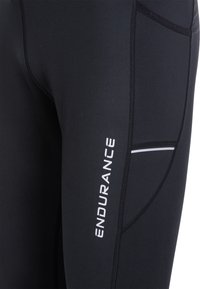 Schwarze Sportleggings mit schlankem Schnitt, Flachnähten, einer Seitentasche und einem reflektierenden Logo-Detail. Glatte Stoffstruktur.