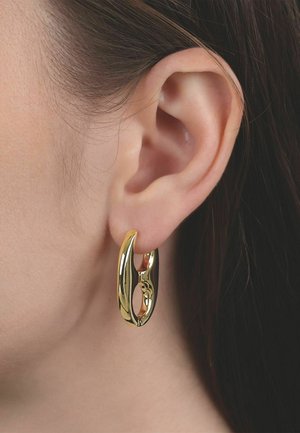 Primo piano dell'orecchio di una persona che indossa un orecchino a cerchio spesso e lucido in oro con un design ovale aperto.