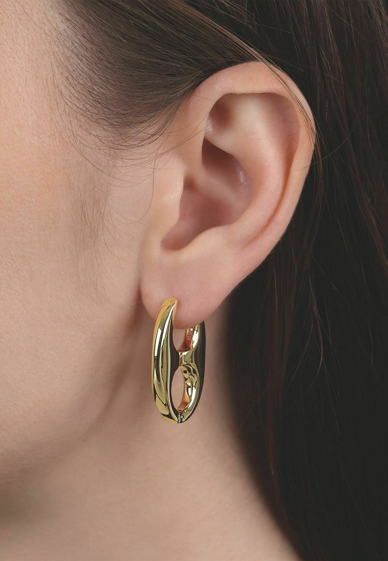 Primer plano de la oreja de una persona que lleva un pendiente de aro grueso y brillante de oro con un diseño ovalado abierto.