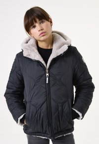 Chaqueta acolchada negra con un forro de capucha beige suave, delantero con cremallera y bolsillos laterales, con tejido texturizado y un bajo adornado.