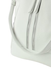 Witte leren tas met textuur, met twee voorritsen en een enkele schouderband, die een gladde afwerking en een minimalistisch ontwerp toont.