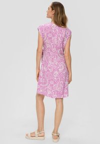 Bloemmotief, knielange jurk in roze met witte accenten; zachte stof, kapmouwen en een ontspannen pasvorm, gecombineerd met lichtgekleurde sandalen.