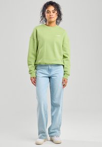 Green sweatshirt with a crew neckline and dropped shoulders, paired with light blue high-waisted jeans and beige sneakers.