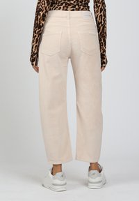 Hellbeige, weite Cordhosen mit zwei Gesäßtaschen, kombiniert mit weißen Sneakern und einem langärmeligen, leopardenmuster Oberteil.