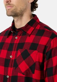 Rood-zwart geblokt shirt van flanel, met een knoopsluiting aan de voorkant, een kraag en een patchzak op de linkerborst.