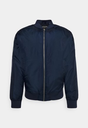 Veste bomber bleu marine avec fermeture éclair argentée à l'avant, col, poignets et ourlet côtelés, présentée sur un fond clair uni.