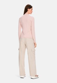 Helles rosa Langarmoberteil kombiniert mit beigen, weiten Cargo-Hosen. Das Oberteil hat einen hohen Kragen; die Hose verfügt über seitliche Taschen und eine strukturierte Oberfläche.