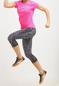 Camisa deportiva texturizada en rosa, leggings capri con patrón en blanco y negro y paneles de malla, y zapatillas de running coloridas con un diseño degradado.