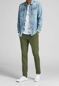 Ljusblå denimjacka över en vit T-shirt, ihop med olivgröna byxor och vita sneakers, med knapplås och dubbla bröstfickor.