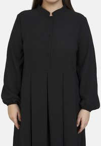Schwarzes Langarmkleid mit Stehkragen, ausgestattet mit einer Knopfleiste und einem gefalteten Rock. Glattes Material mit gerafften Ärmeln.