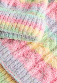 Manta de punto multicolor que presenta tonos pastel de rosa, amarillo, verde y lavanda en un patrón de cable texturizado con lana esponjosa.