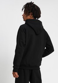 Sudadera con capucha negra de corte relajado, con puños y dobladillo acanalados. Textura suave, sin logotipos ni patrones visibles, diseño liso.