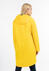 Gul vandtæt jakke med hætte, der har lange ærmer og strækker sig til midten af låret. Glat tekstur med minimale syningdetaljer.