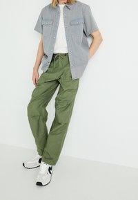 Maglietta a maniche corte grigia con bottoni, t-shirt bianca sotto, pantaloni cargo verde oliva e sneakers nere/bianco con suola testurizzata.