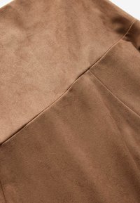 Hnědá umělá semišová látka s hladkým texturem, ukazující švy a jemné variace v odstínu pro hloubku. Vhodná pro oděvy nebo doplňky.