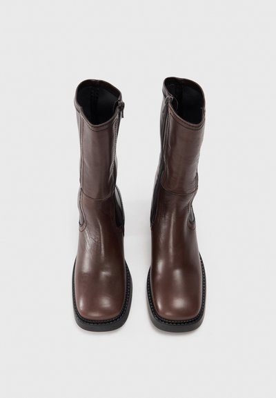 Bottines en cuir marron avec un bout arrondi, fermeture éclair latérale, accents en élastique et semelle en caoutchouc noir texturé. Finition lisse et détails de couture.