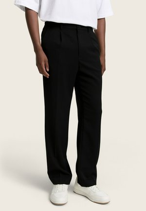 Pantalones negros a medida con una tela suave, diseño de pierna recta y sutiles rayas verticales; combinados con zapatillas blancas.