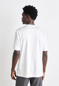 Tricou alb cu mânecă scurtă, având guler rotund, croială lejeră, textură netedă și fante laterale la tiv pentru un plus de confort în mișcare.