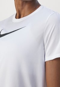Vit Nike sport t-shirt med en svart swoosh-logotyp. Den har rund halsringning och kort ärm, tillverkad av ett slätt, andningsbart tyg.
