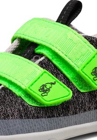 Zapatilla texturizada en negro y gris con tiras de Velcro y acentos en verde neón. Presenta un logotipo en relieve en la tira. Suela de goma, vista en primer plano.