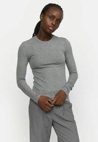 Maglioncino grigio chiaro a maniche lunghe realizzato in tessuto morbido, con scollo rotondo e taglio aderente, abbinato a pantaloni grigi eleganti.