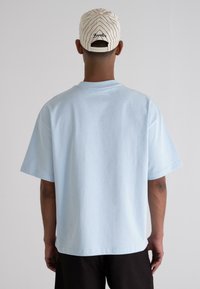 Light blue cotton t-shirt with short sleeves and a crew neckline, featuring a relaxed fit. Back of a beige cap with diagonal stripes and "Berlin" logo.